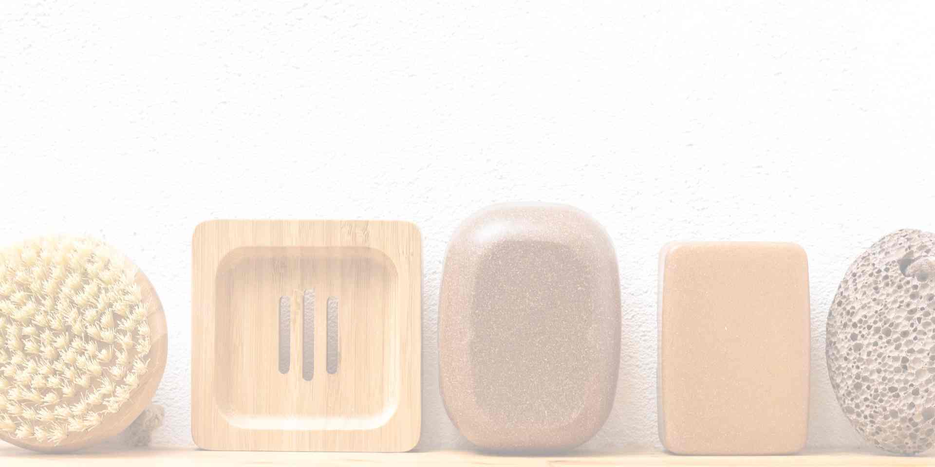 Aufgereiht eine Massagebürste, Bambusseifenunterlage, dunkle Seifendose, helle Seifendose und ein Lavastein