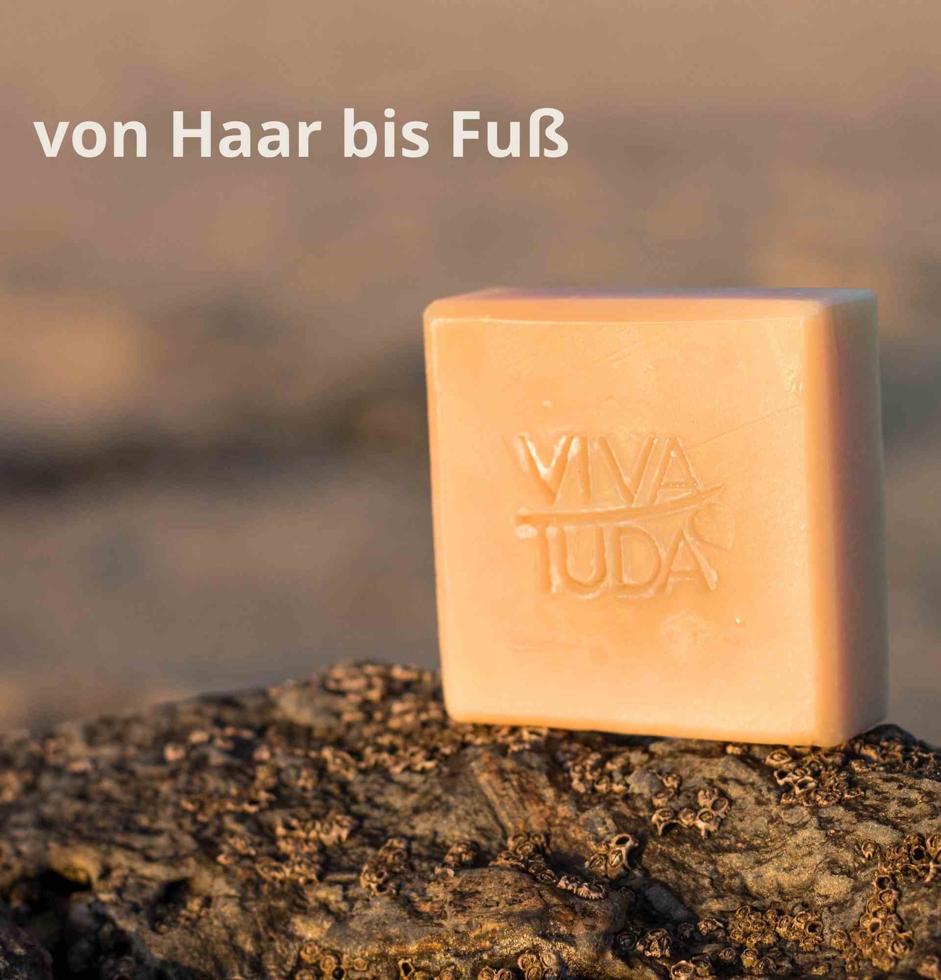 Helle, quadratische Naturseife mit VIVA TUDA Stempel auf einem Stein in der Sonne.