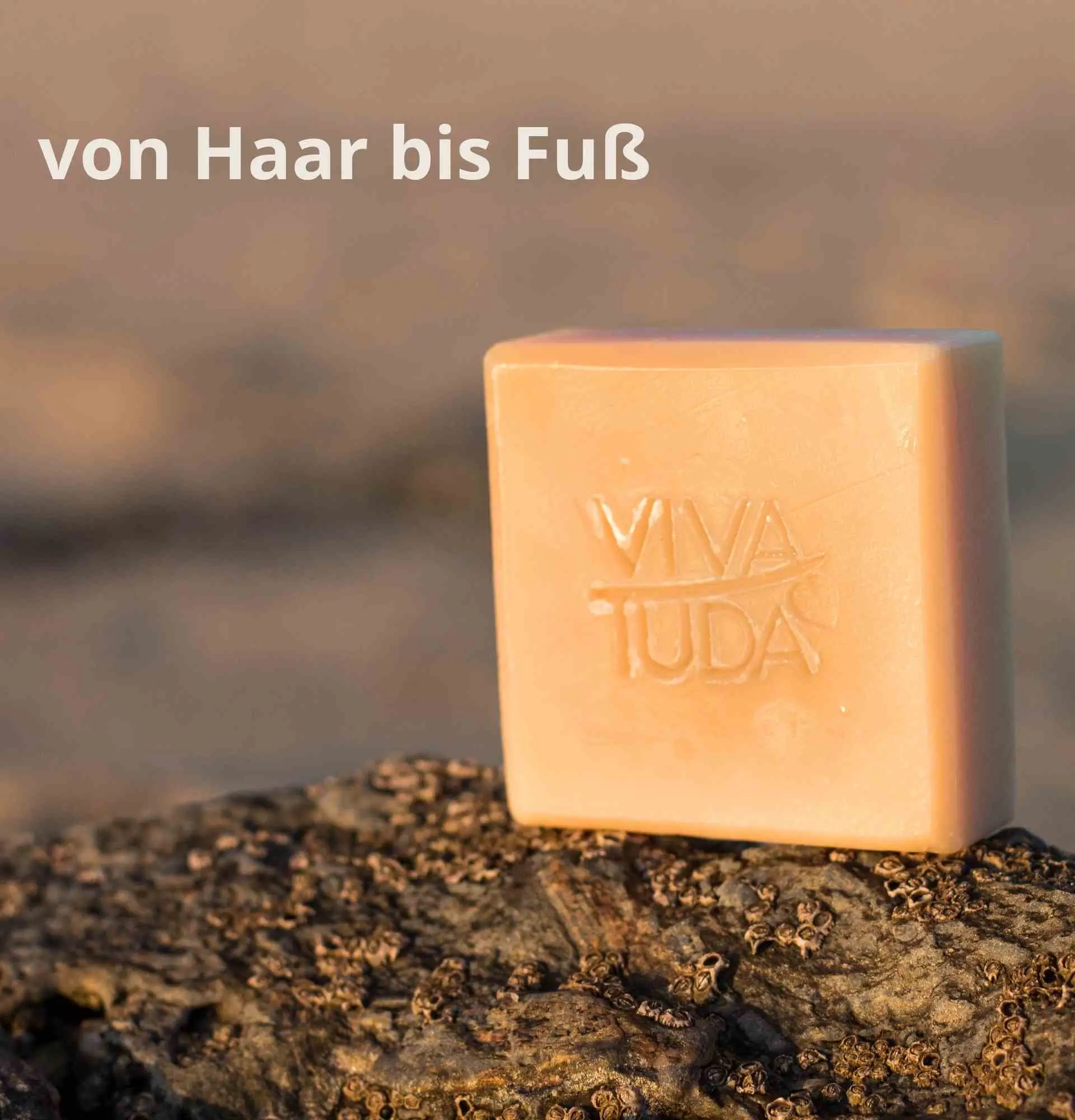 Helle, quadratische Naturseife mit VIVA TUDA Stempel auf einem Stein in der Sonne.