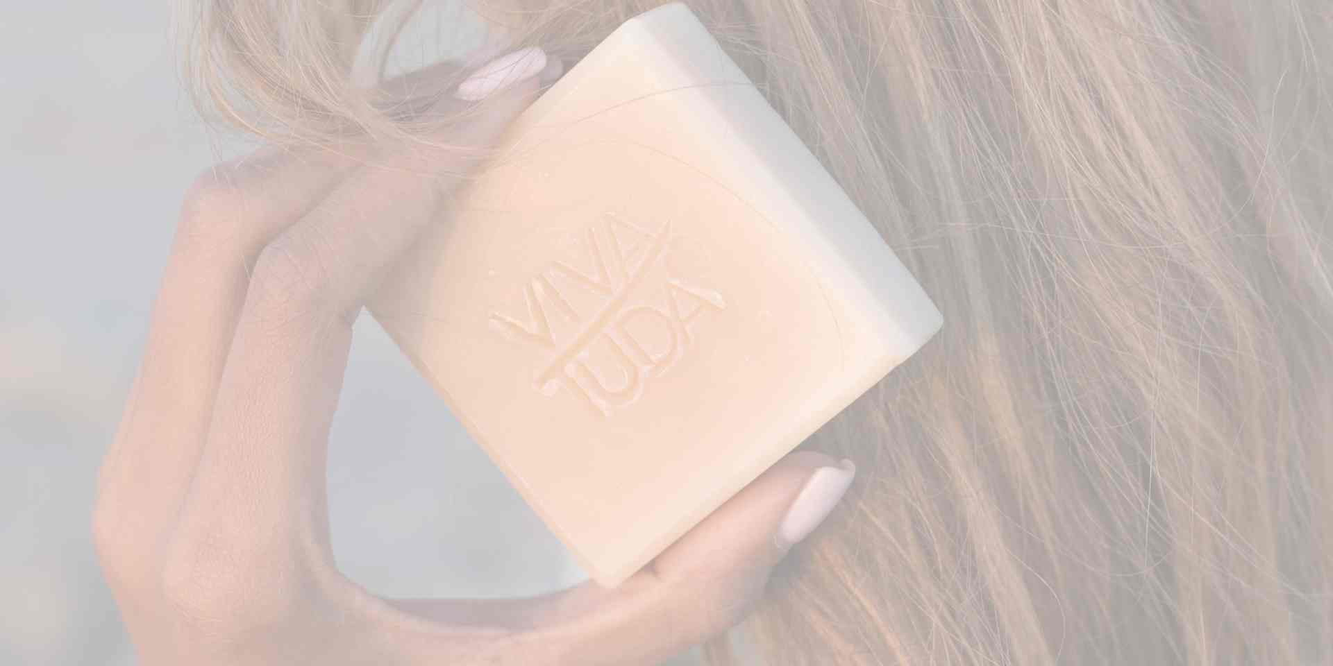 Helle Shampooseife wird mit einer Hand an dunkel blondes Haar gehalten