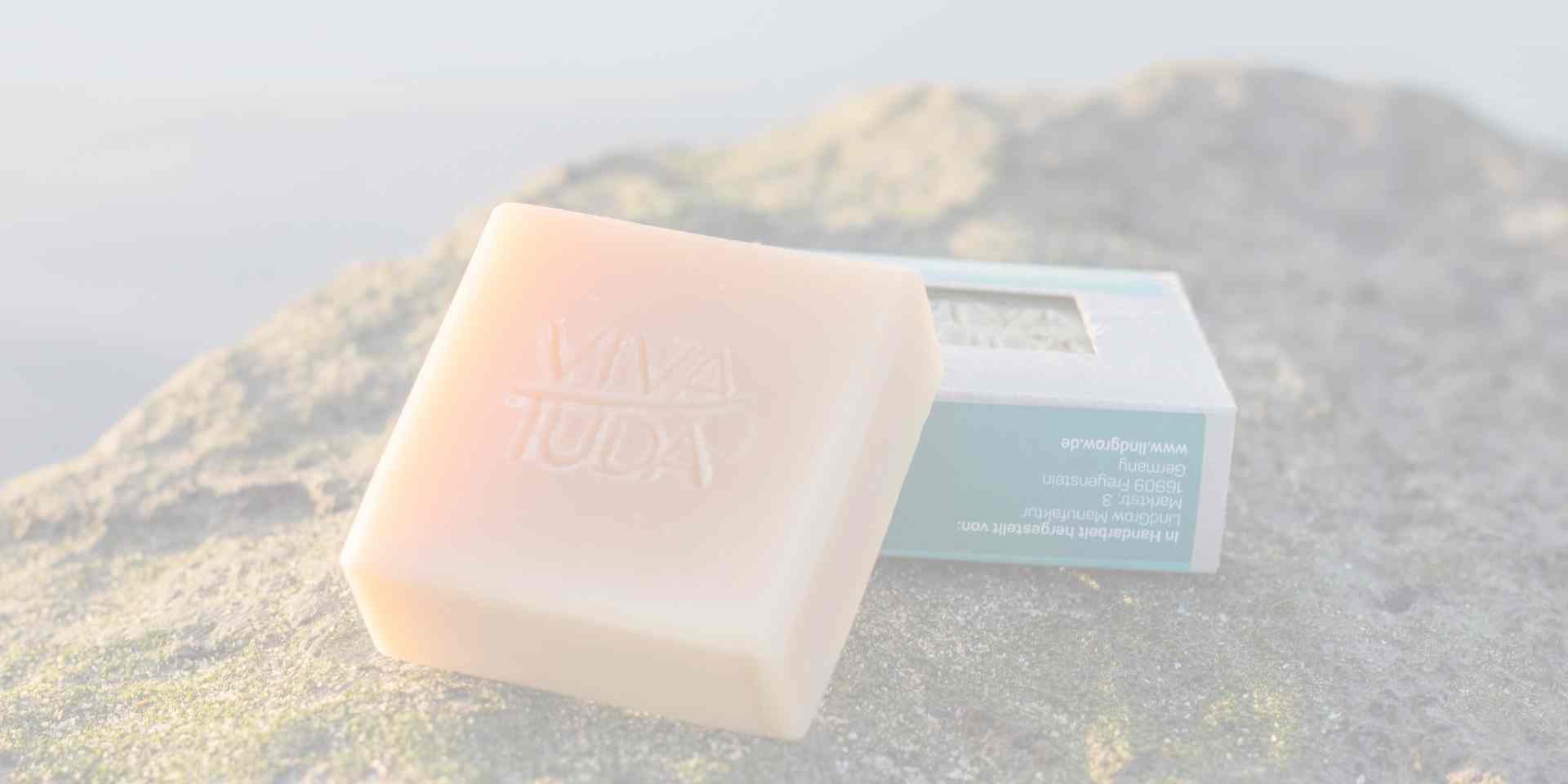 Helle Seife im Vordergrund Kartonverpackung im Hintergrund Steine