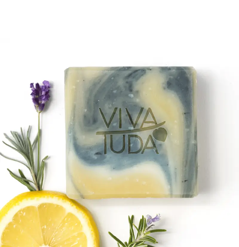 Sonniger Süden Naturseife, blau-grün und gelb marmoriert. Daneben Rosmarin und eine Zitronenscheibe.