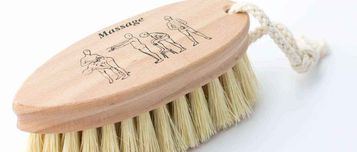 Eine Holzbürste mit hellen Borsten und weißer Kordel. Mit Massageanleitung auf dem Rücken.